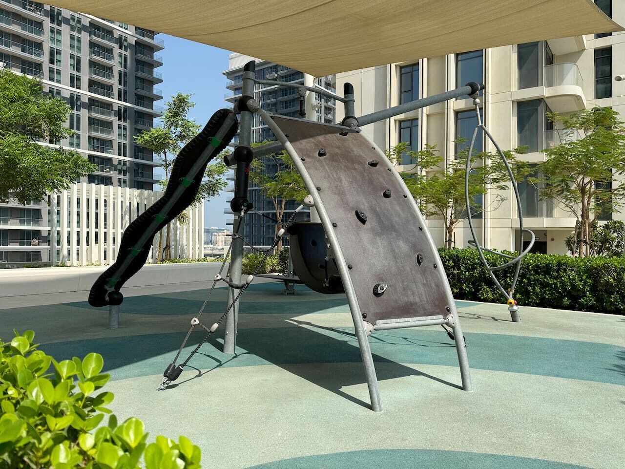 A playground with a slide and climbing structure, surrounded by buildings and greenery.