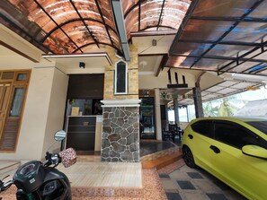 A hotel entrance with a stone pillar, a reception desk, and a yellow car parked outside. - FATHIN HOTEL BAWEAN SYARIAH (Sangkapura)