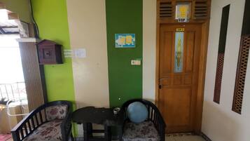 Una habitación con pared verde y blanca, una puerta de madera con un letrero que dice 'VIP 2', dos sillas con tapicería floral y una mesita con un frutero.