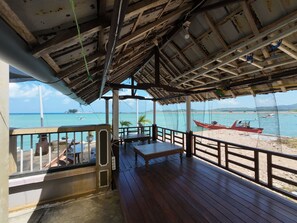 A wooden deck with a view of the sea, a red boat, and a clear sky. - FATHIN HOTEL BAWEAN SYARIAH (Sangkapura)