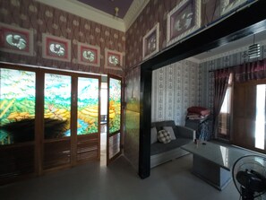 A room with a sofa, a fan, and a wall with patterned wallpaper.