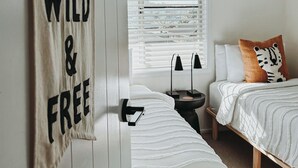 Ein Schlafzimmer mit zwei Betten, einem Deckenventilator, einem Fenster mit Jalousien und einem an der Wand befestigten Schild mit der Aufschrift 'WILD & FREE'.