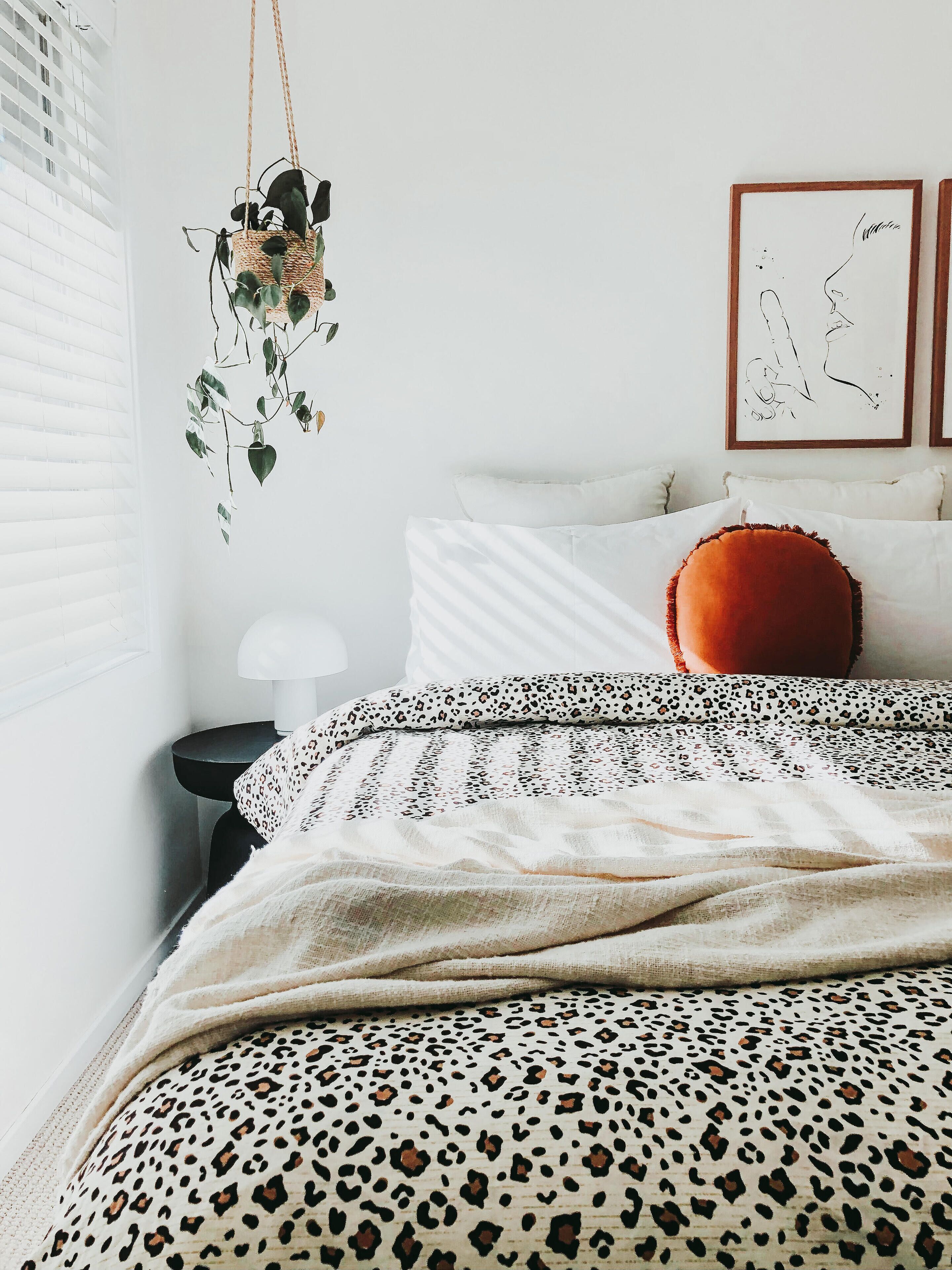 Een slaapkamer met een bed, kussens, een hangplant en kunst aan de muur.