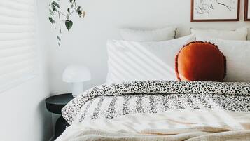 Een slaapkamer met een bed, kussens, een hangplant en kunst aan de muur.