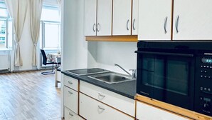 A kitchen with white cabinets, a black microwave, and a double sink. - Modern Studio Stay Near Stadthalle (Vienna)