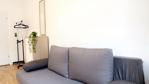 A grey sofa in a room with a wooden floor, a hanging plant, a mirror, and a coat rack. - Modern Studio Stay Near Stadthalle (Vienna)