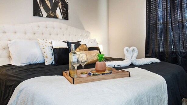 Una cama bien hecha con edredón blanco, una bandeja de madera con una botella, un vaso y libros.