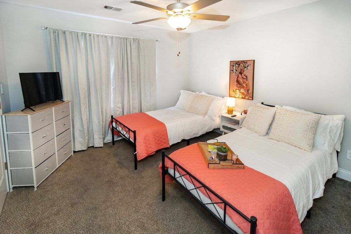 Habitación de hotel con dos camas, televisión, escritorio y ventilador de techo.