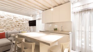 A modern kitchen with a stone wall, a large island with bar stools, and a flat-screen TV mounted above the island.