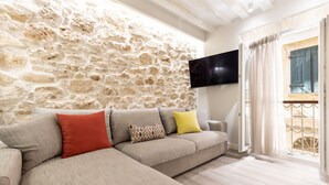 A living room with a stone wall, a flat-screen TV mounted on it, a beige sofa with cushions, and a wooden floor.