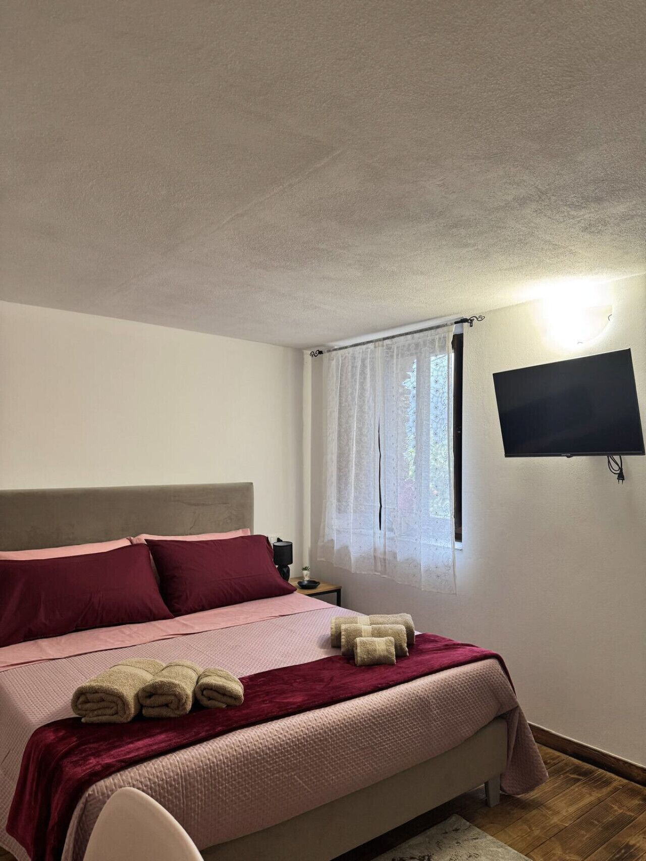 Une chambre à coucher avec un lit, un téléviseur fixé au mur et une fenêtre avec des rideaux.
