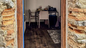 A narrow doorway leading into a room with a rustic brick wall, a wooden floor, a small table with a chair, and a desk with a computer and other items. - B&B Nonna Cristina - Double Room 1 (Vecchio Abitato)