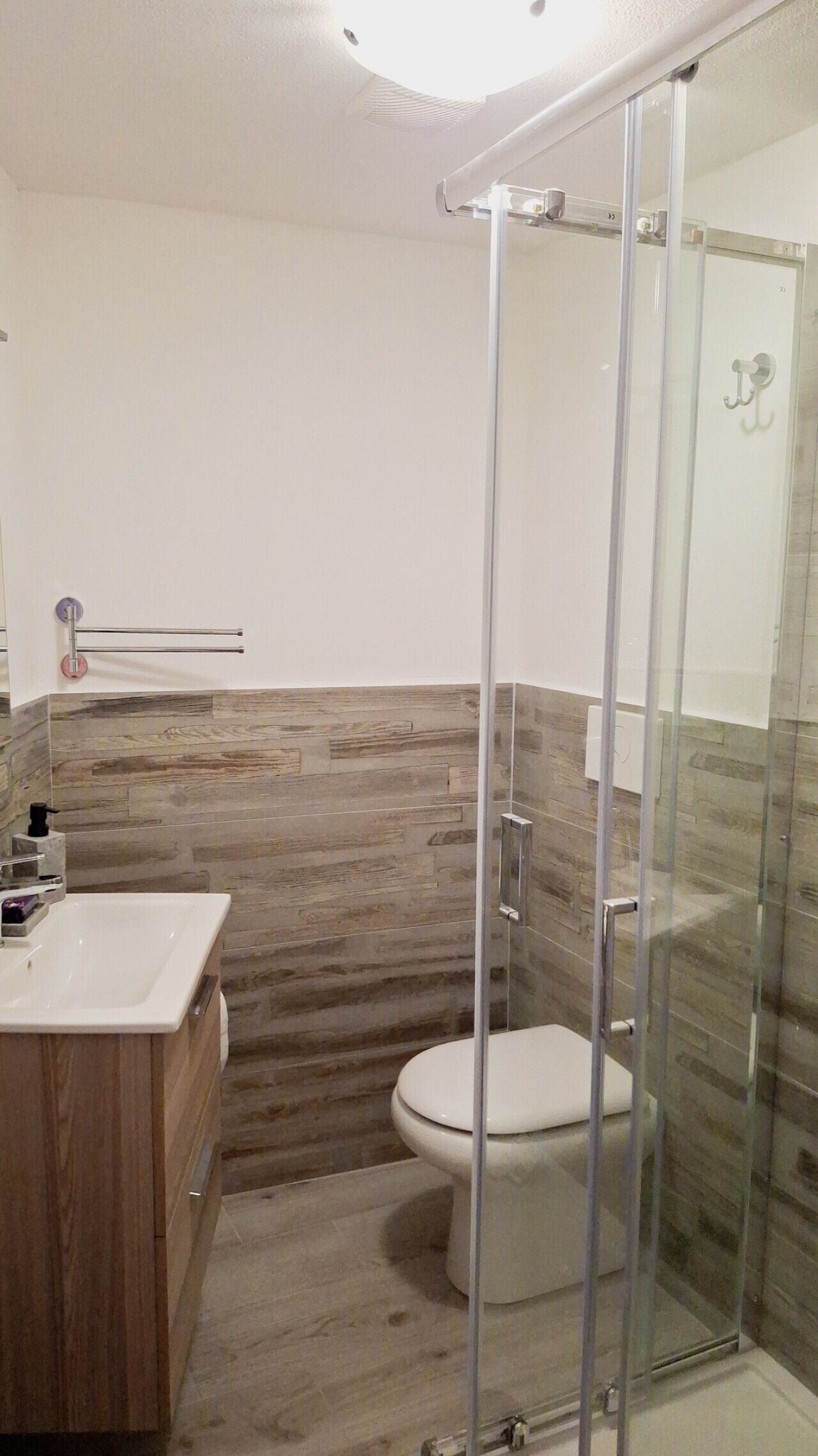 A modern bathroom with a glass shower enclosure, a wooden vanity, and a toilet.