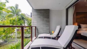 A balcony with two lounge chairs, a small table with a glass, and a view of tropical greenery. - Elegant Beachfront 3BR Condo at Pearl of Naithon (Sa Khu)