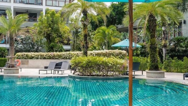 A swimming pool with a tiled surface, surrounded by lounge chairs and a large umbrella. - Elegant Beachfront 3BR Condo at Pearl of Naithon (Sa Khu)