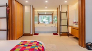 A hotel room with a large bed, a view of the bathroom, and a wooden wardrobe. - Elegant Beachfront 3BR Condo at Pearl of Naithon (Sa Khu)