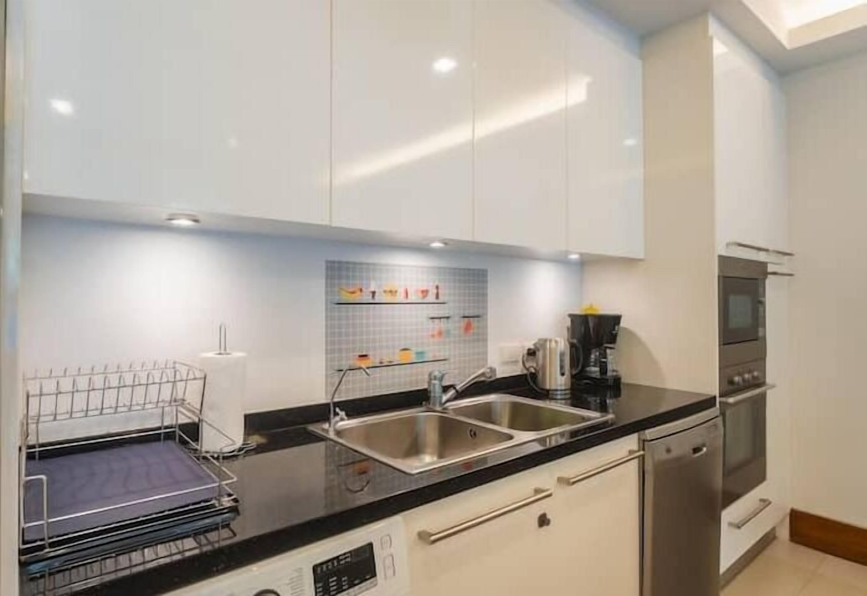 Una cocina moderna con armarios blancos, encimera negra, pileta de acero inoxidable y cafetera.