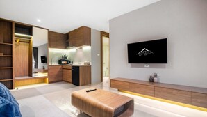 A modern living room with a wooden bench, a TV mounted on the wall, and a kitchen area with wooden cabinets and a built-in oven. - Beachfront 1501 2BR at Wyndham Naithon Phuket (Sa Khu)