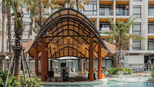 A pool area with a wooden gazebo, palm trees, and a modern building in the background. - Beachfront 1501 2BR at Wyndham Naithon Phuket (Sa Khu)