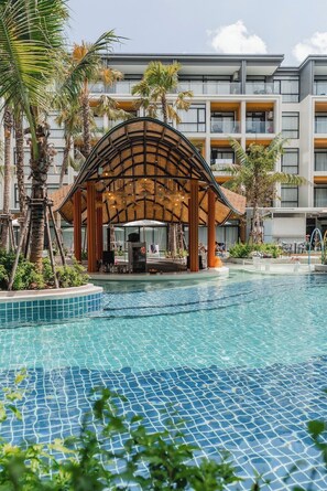 A pool area with a wooden gazebo, palm trees, and a modern building in the background. - Beachfront 1501 2BR at Wyndham Naithon Phuket (Sa Khu)