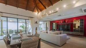 A spacious living area with a dining table, sofa, and a large flat-screen TV mounted on a red wall. - Luxury 3BR Villa 5 Private Pool, Gym & Jacuzzi (Choeng Thale)
