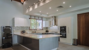 A modern kitchen with a central island, stainless steel appliances, and a large window providing natural light. - Luxury 3BR Villa 5 Private Pool, Gym & Jacuzzi (Choeng Thale)