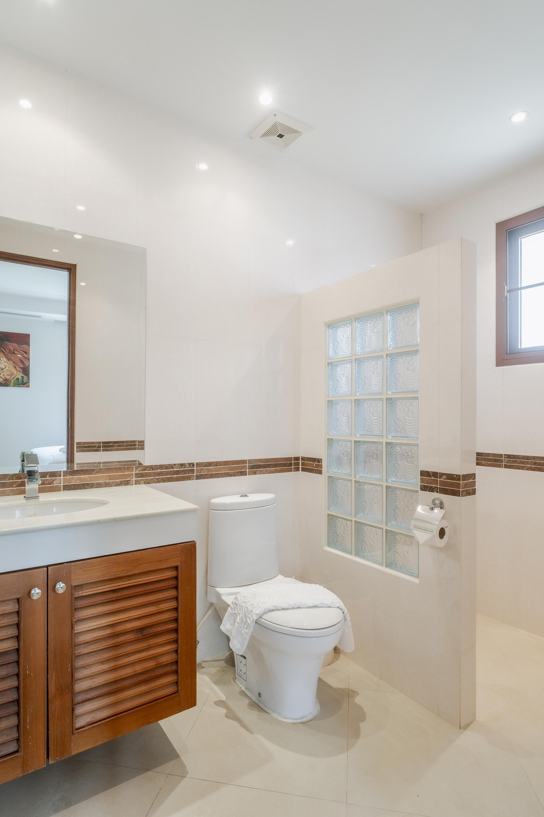 A bathroom with a wooden vanity, a white toilet, and a glass shower enclosure.