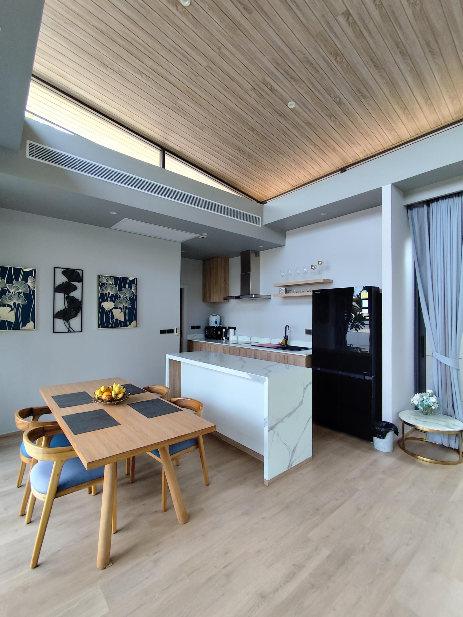 A modern kitchen with a marble island, wooden ceiling, and a dining area with a table and chairs.