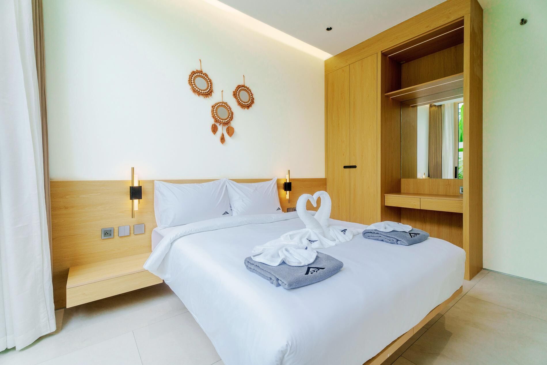 Una cama bien tendida con sábanas blancas, cabecera de madera y lámpara fijada a la pared.