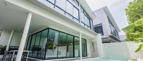 A modern two-story house with a glass-enclosed patio and a swimming pool.
