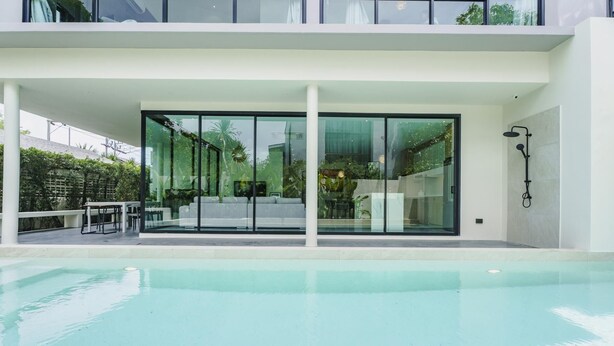 A modern building with a swimming pool, large glass doors, and outdoor seating. - Harmony Exclusive Villa, Bang Tao Phuket (Choeng Thale)