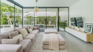 A modern living room with a large sofa, a coffee table, and a TV on a white cabinet. - Harmony Exclusive Villa, Bang Tao Phuket (Choeng Thale)