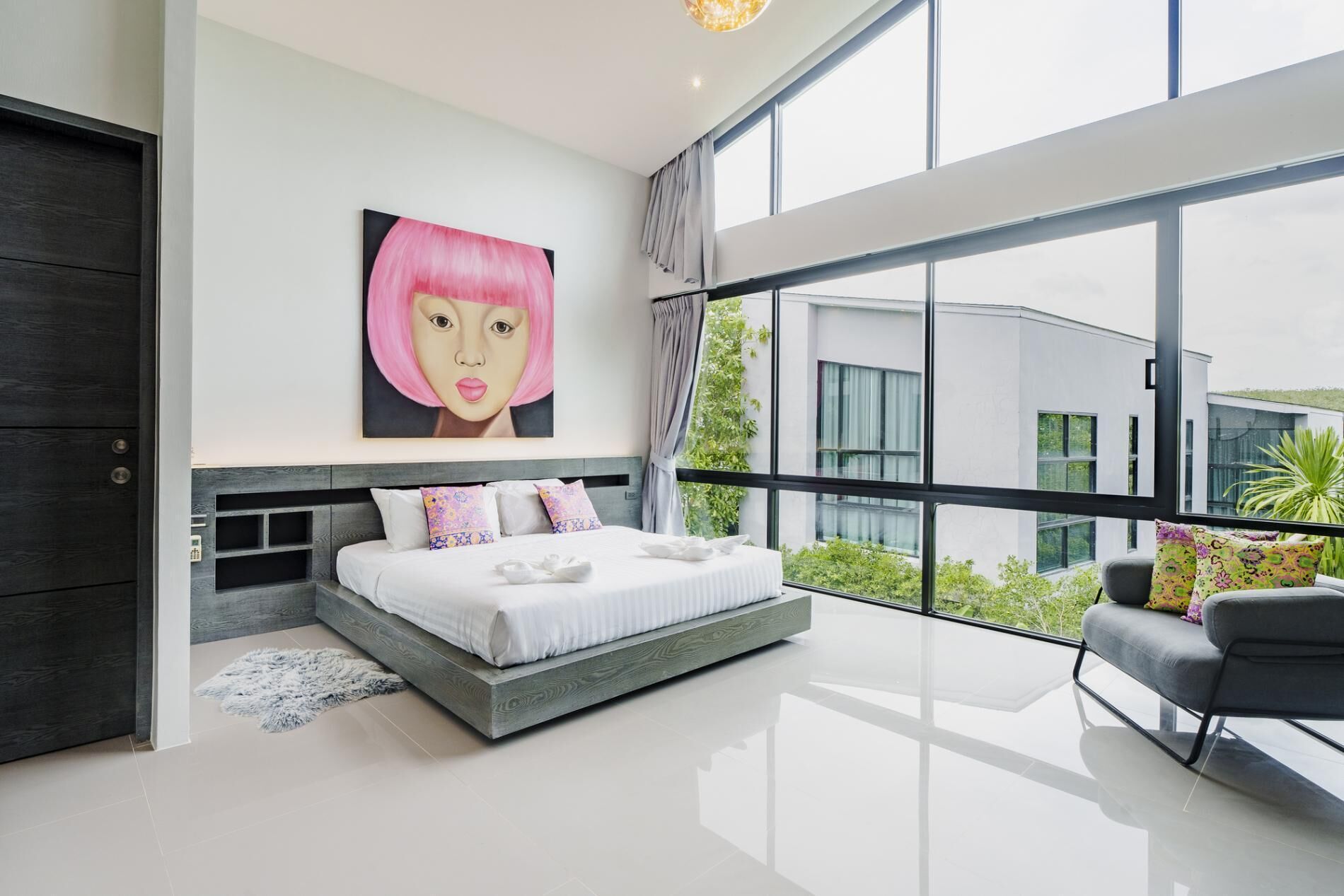 A modern bedroom with a large bed, a view of greenery outside, and a painting on the wall.