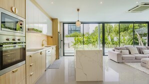 A modern kitchen with a large island, built-in appliances, and a view to a lush garden. - Harmony Exclusive Villa, Bang Tao Phuket (Choeng Thale)