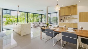 A modern kitchen with a dining area, large windows, and a view of greenery. - Harmony Exclusive Villa, Bang Tao Phuket (Choeng Thale)