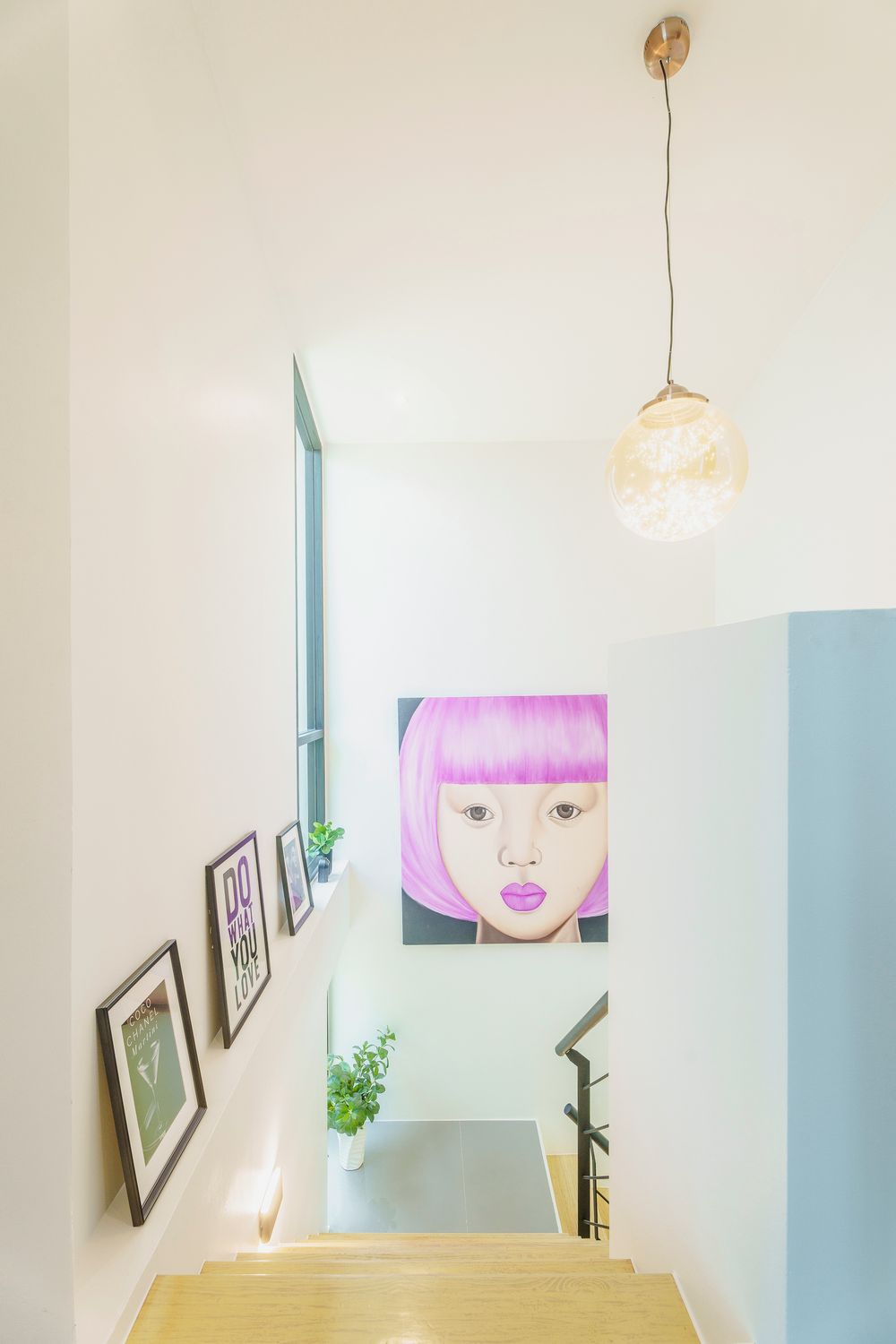 A staircase with a wooden handrail, a wall-mounted light fixture, and framed pictures.