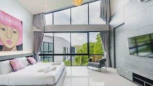 A modern bedroom with a large bed, a TV, and a view of greenery outside. - Harmony Exclusive Villa, Bang Tao Phuket (Choeng Thale)