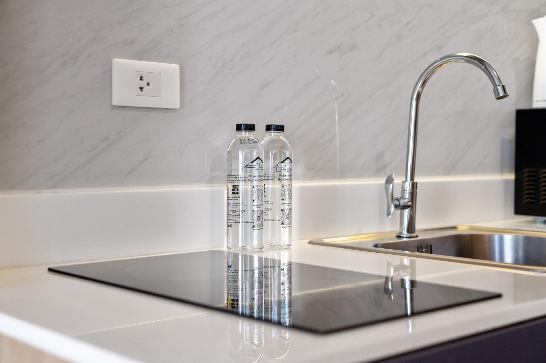 A modern kitchen with a marble backsplash, a stainless steel sink, and two clear water bottles on a black countertop.