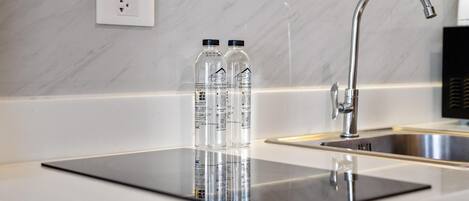 A modern kitchen with a marble backsplash, a stainless steel sink, and two clear water bottles on a black countertop.