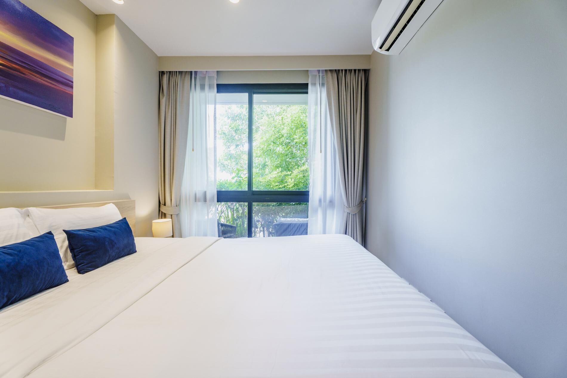 A hotel room with a large bed, a window with curtains, and an air conditioning unit.