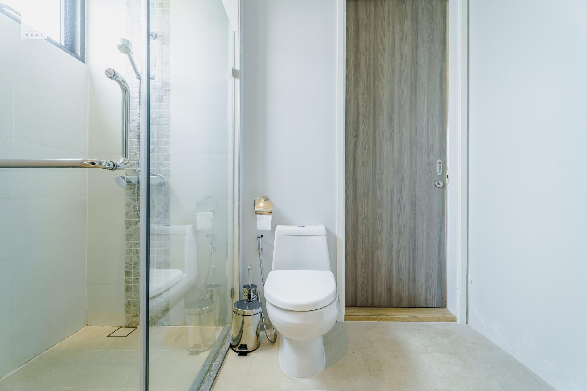 A modern bathroom with a glass shower enclosure, a toilet, and a wooden door.