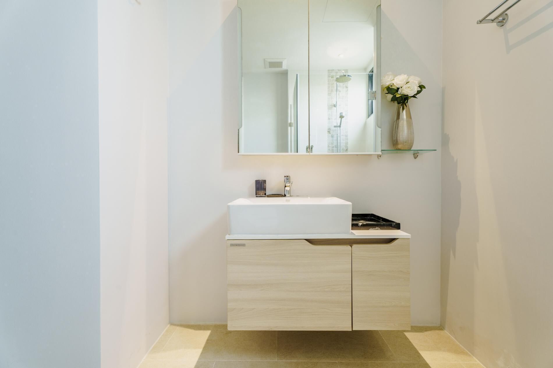 Een moderne badkamer met een wit wastafelmeubel, een spiegel en een vaas met bloemen op een plank.