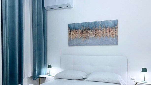 Ein modernes Hotelzimmer mit einem weißen Bett, türkisblau gestreuter Bettwäsche und einem Bild an der Wand.