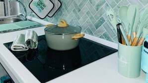 Eine moderne Küche mit einer schwarzen Induktionskochplatte, einem grünen Topf und einem Set aus Holzkocherutensilien in einem hellblauen Behälter.