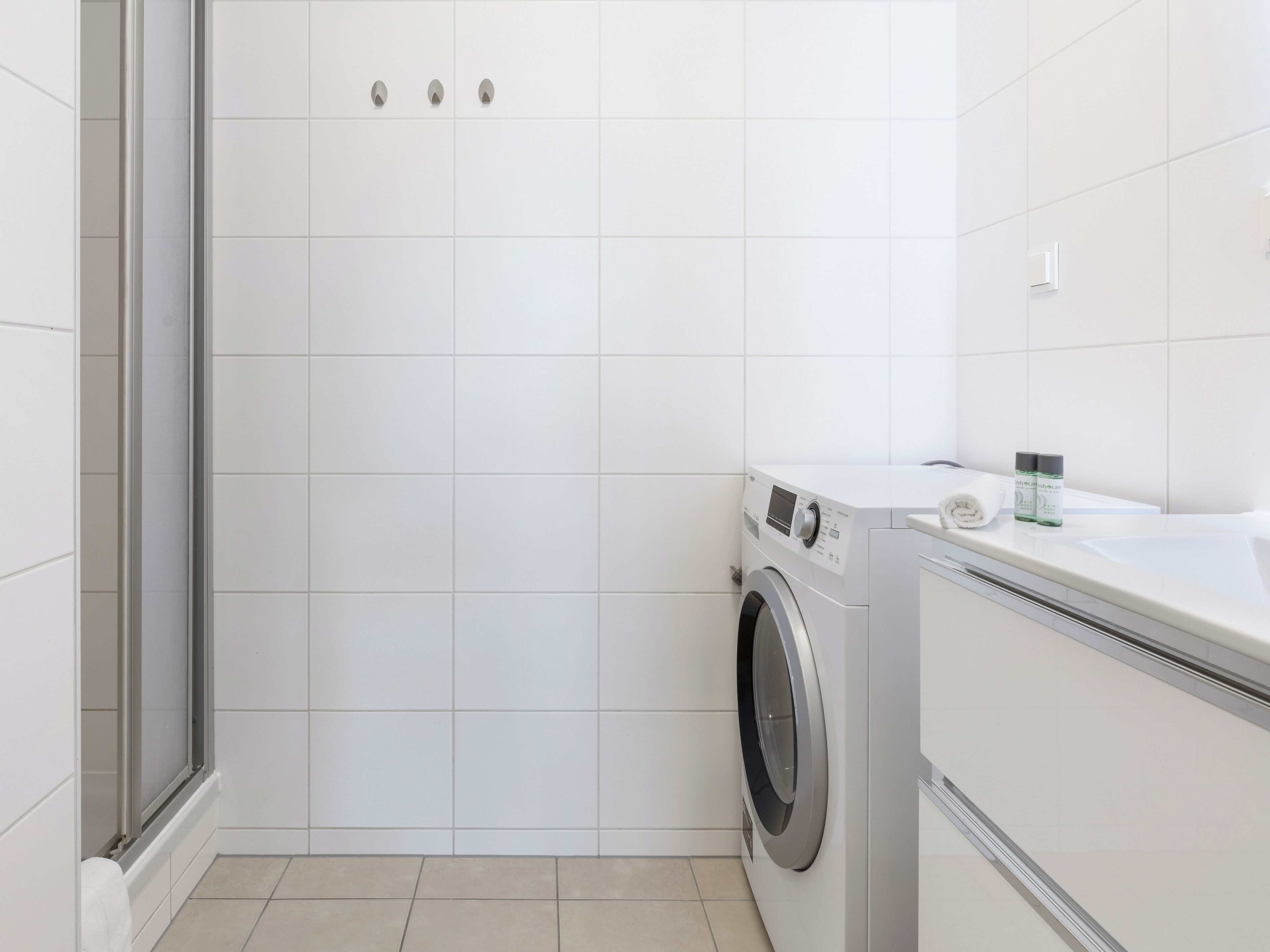 Ein modernes Badezimmer mit Duschkabine aus Glas, einer integrierten Waschmaschine und einem weißen Waschbecken.