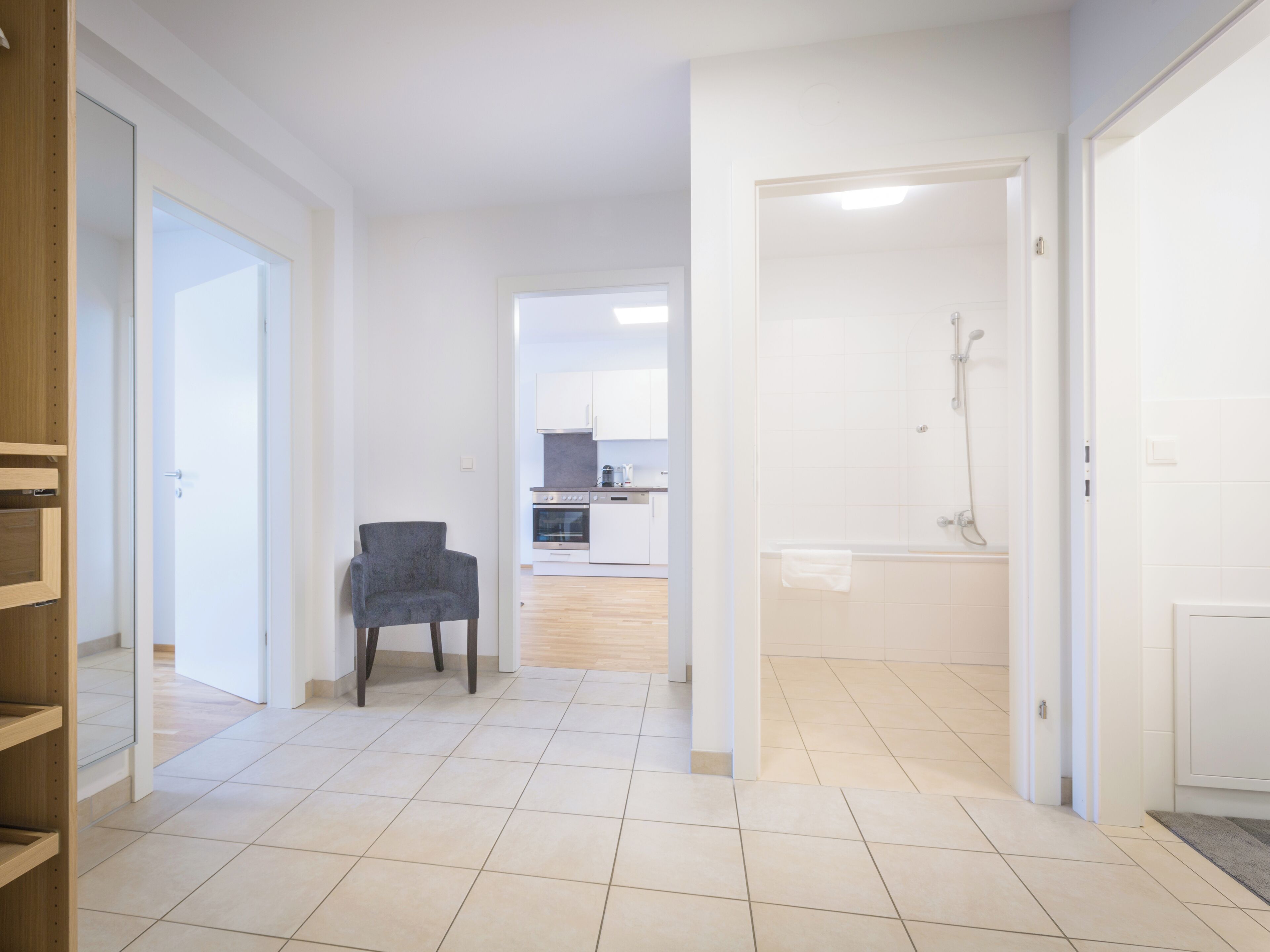 Un'ampia zona giorno con una poltrona grigia, una cucina sullo sfondo e un bagno con doccia.