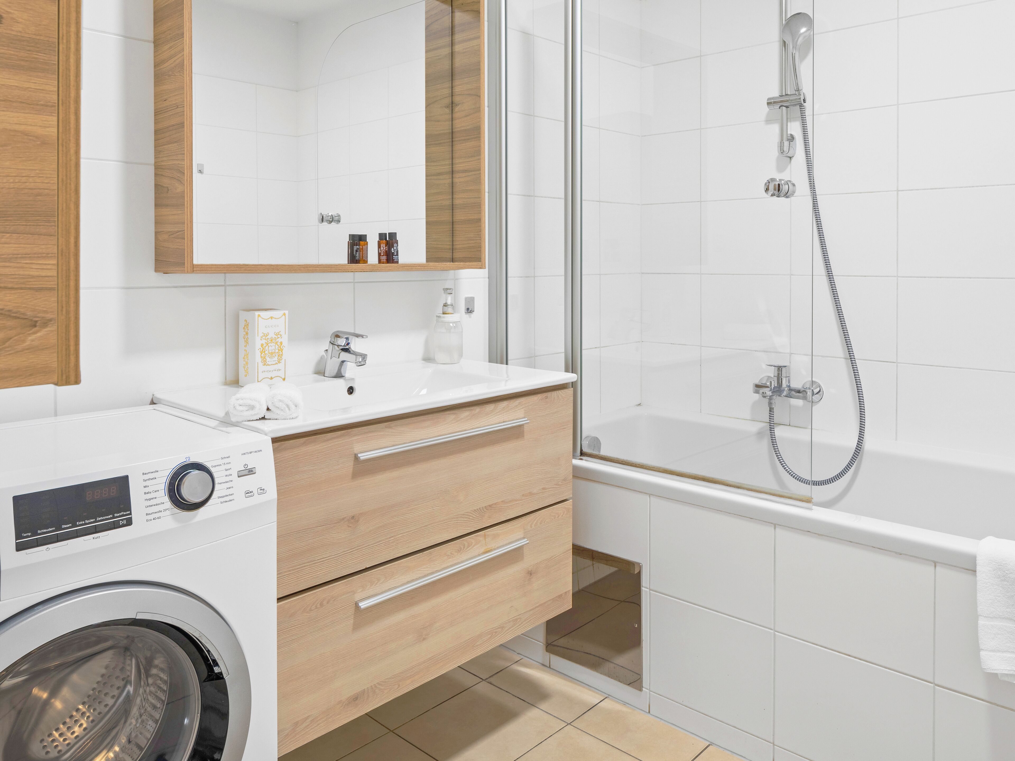 A modern bathroom with a washing machine, a sink with toiletries, and a glass-enclosed shower area.