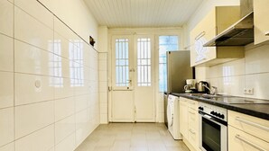 Una cocina estrecha con paredes de azulejos blancos, un par de puertas, una lavadora, una estufa y un lavamanos.