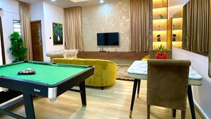 A modern living room with a pool table, a sofa, a dining table, and a TV. - Serviced Apartment (Lekki)