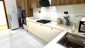 A modern kitchen with wooden cabinets, a built-in stove, and a stainless steel sink. - Serviced Apartment (Lekki)